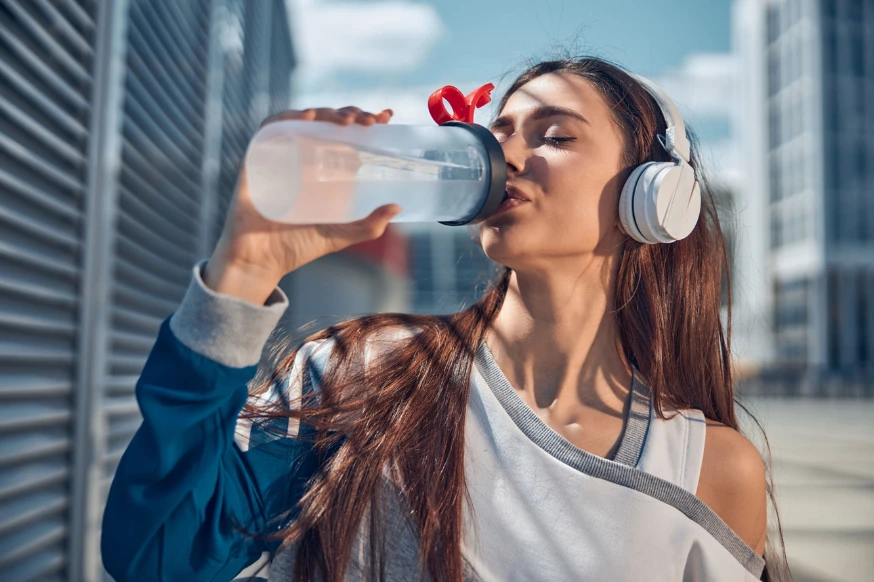 Woman drinking water from a flask while walking